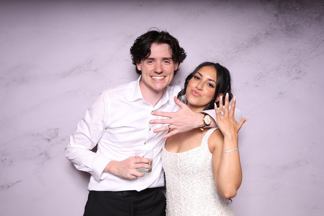 Two people posing in front of a pale purple backdrop, showing rings