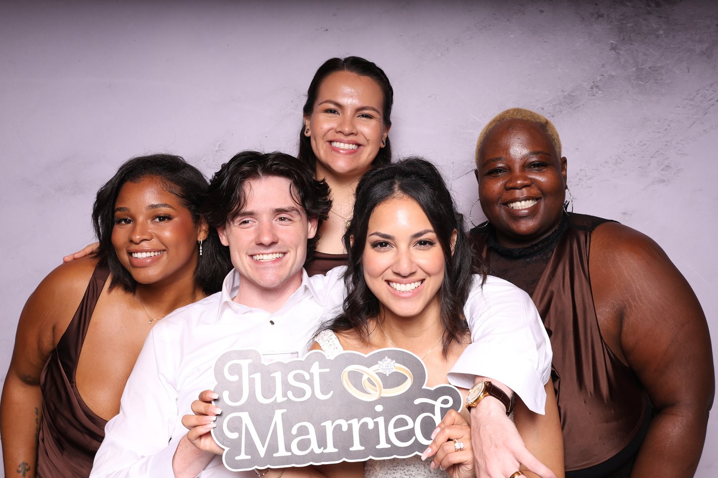 A group of friends holding a Just Married sign in front of a marble backdrop