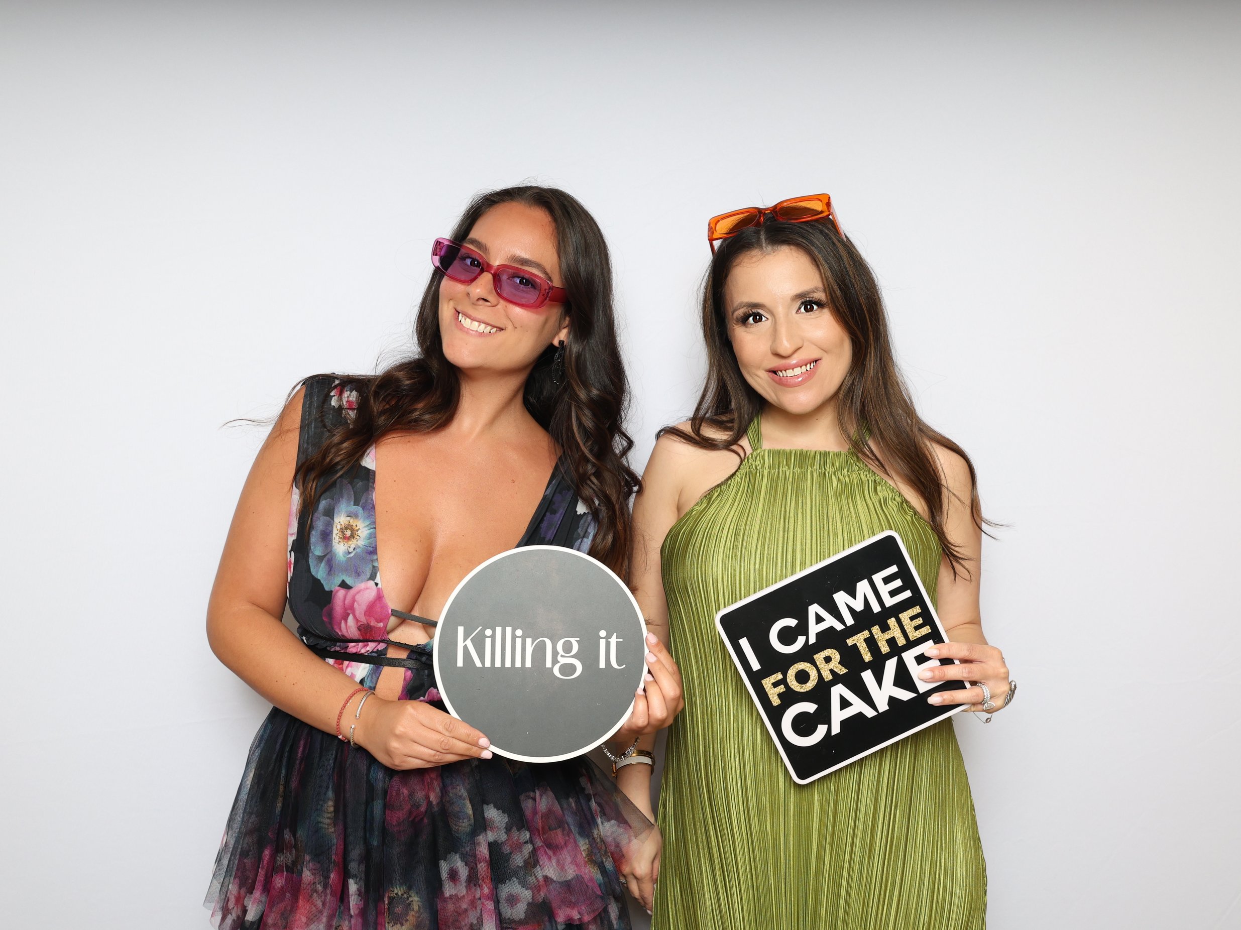 Two women in sunglasses holding sign props that read Killing it and I came for the cake